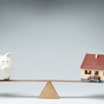 Model house and piggy bank balancing on a seesaw